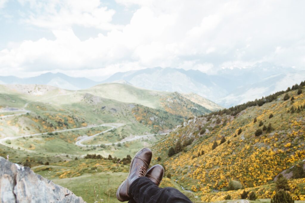 person wearing brown leather boots near mountains at daytime