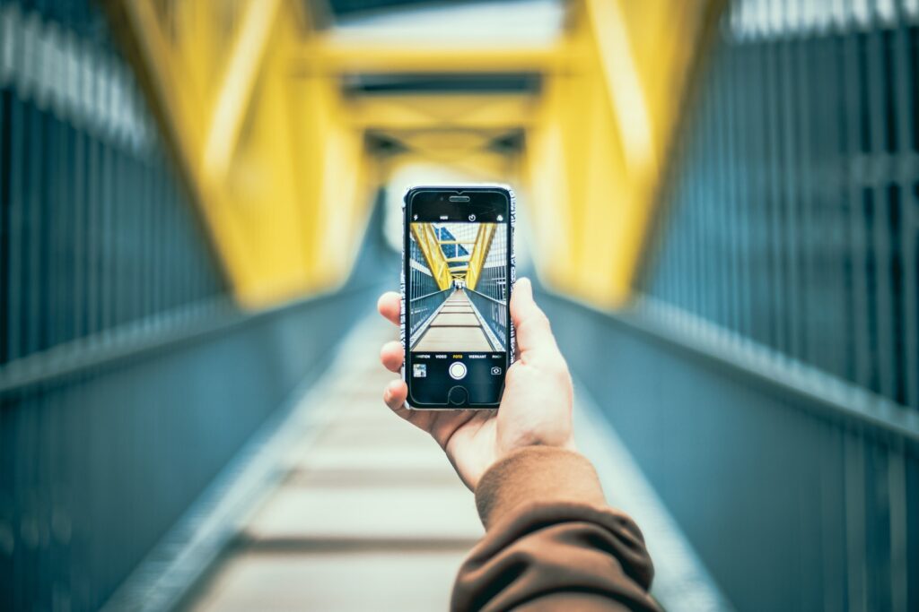 selective focus photo of person holding space gray iPhone 6 taking a photo of a bridge