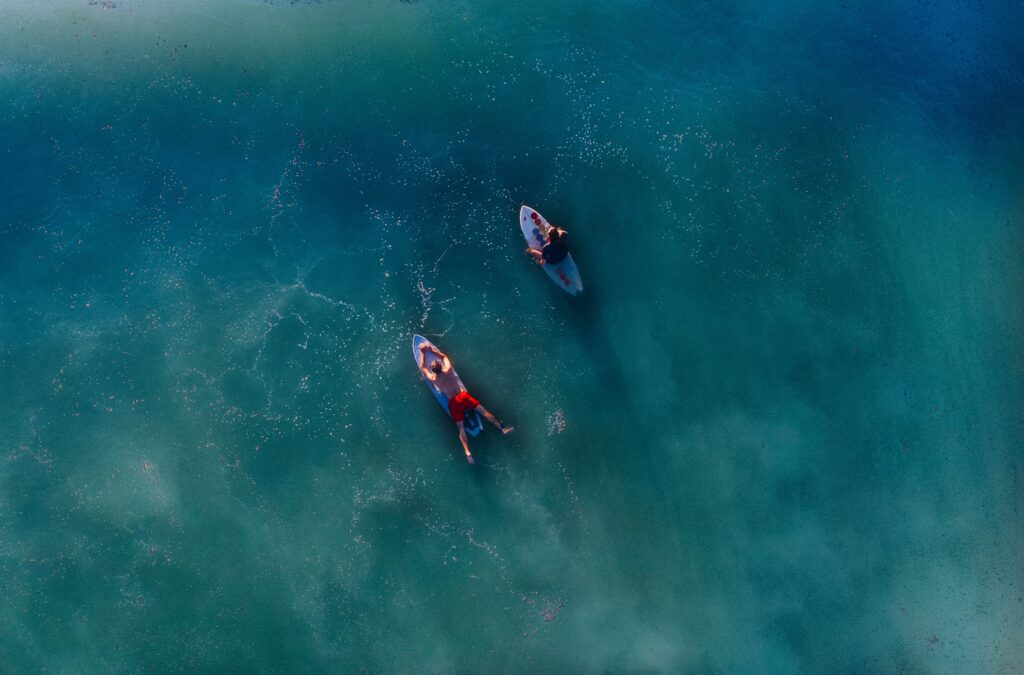 top view photography of two persons on blue surfboard at daytime